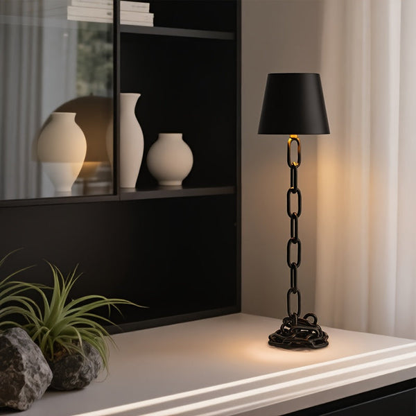 Abajur de mesa com estrutura de corrente de metal preta aceso sobre uma mesa