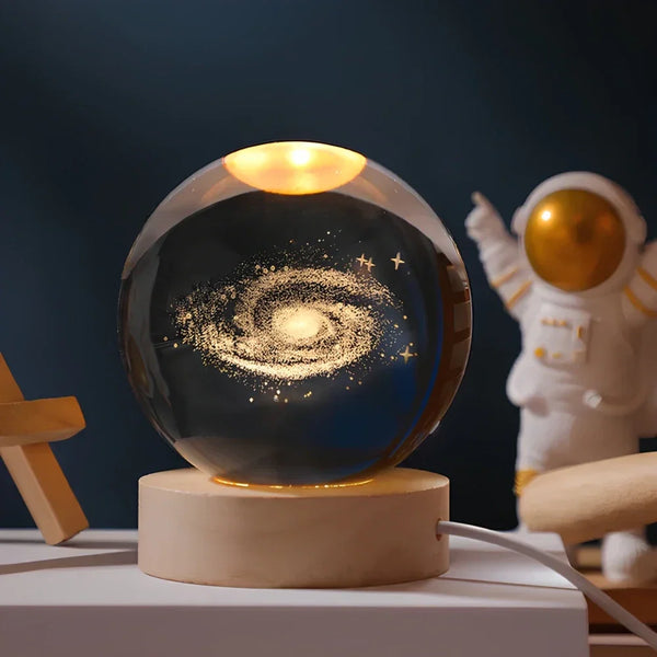Abajur em esfera acesa sobre base, com gravação tridimensional visível no interior