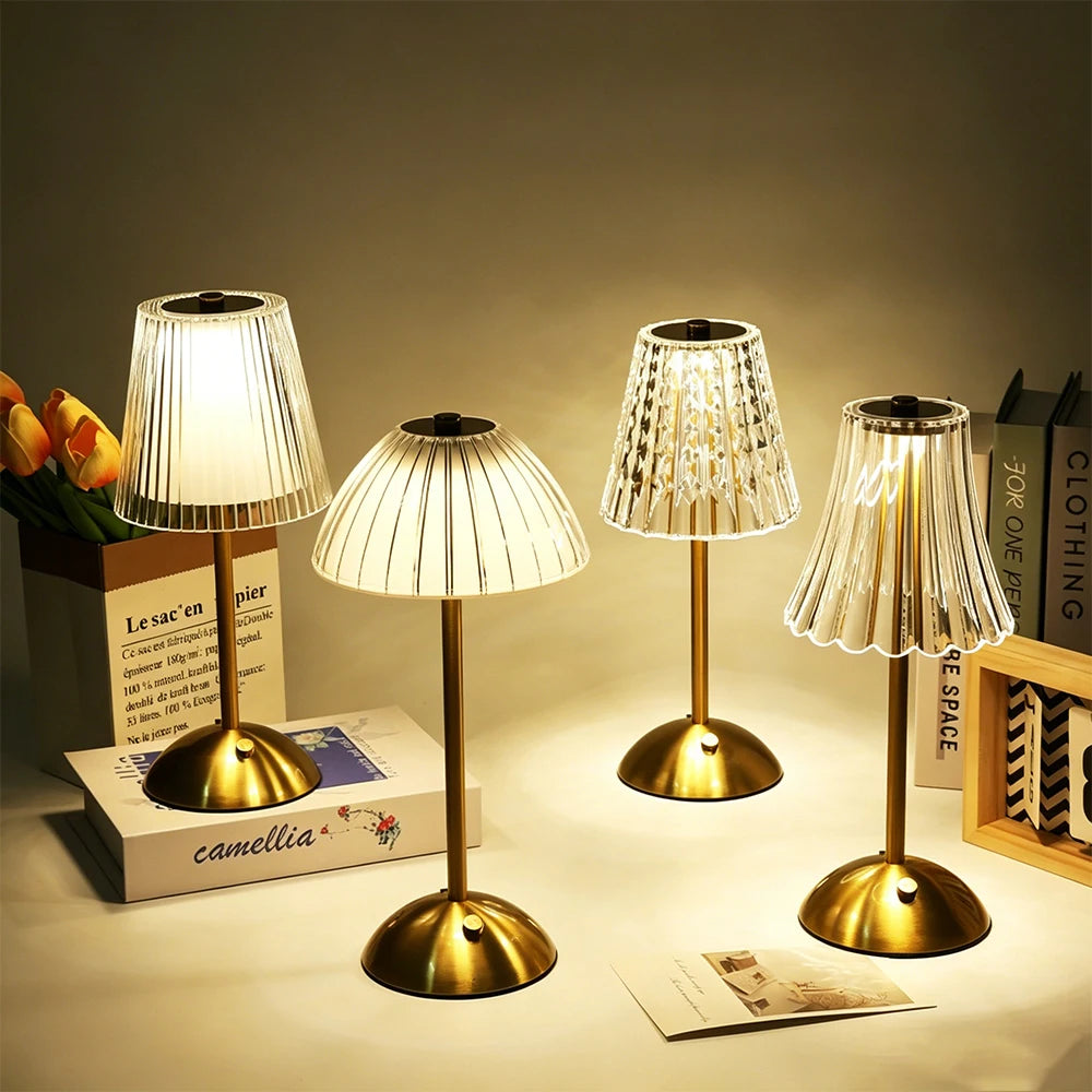 Abajur de cristal com base dourada aceso sobre um criado-mudo, refletindo pontos de luz