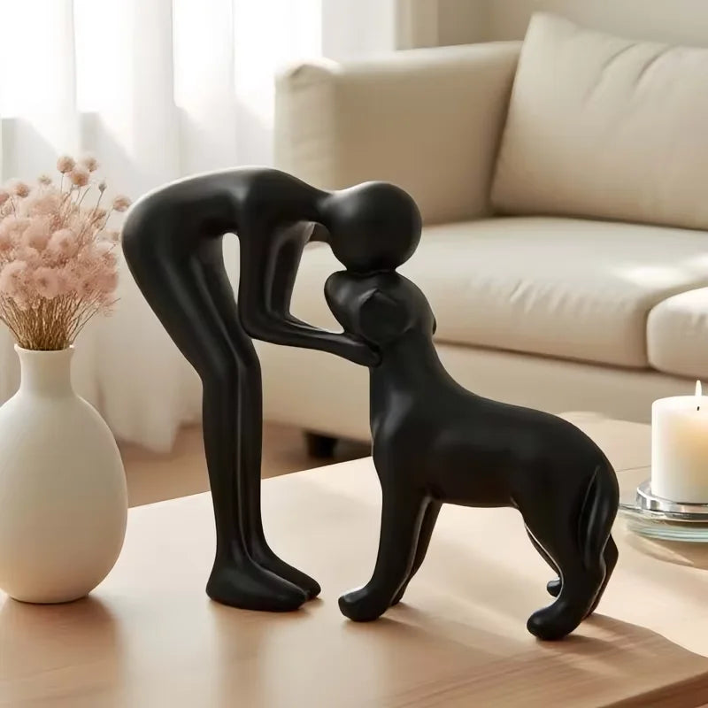 Escultura abstrata preta de homem abraçando um cachorro sobre a mesa