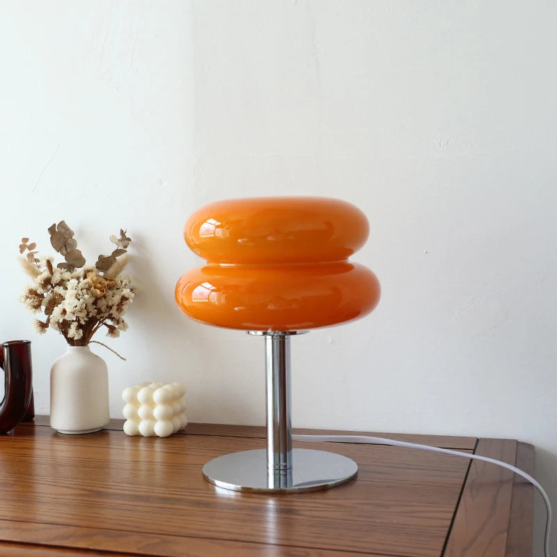 Luminária de mesa com cúpula de vidro laranja acesa sobre o aparador