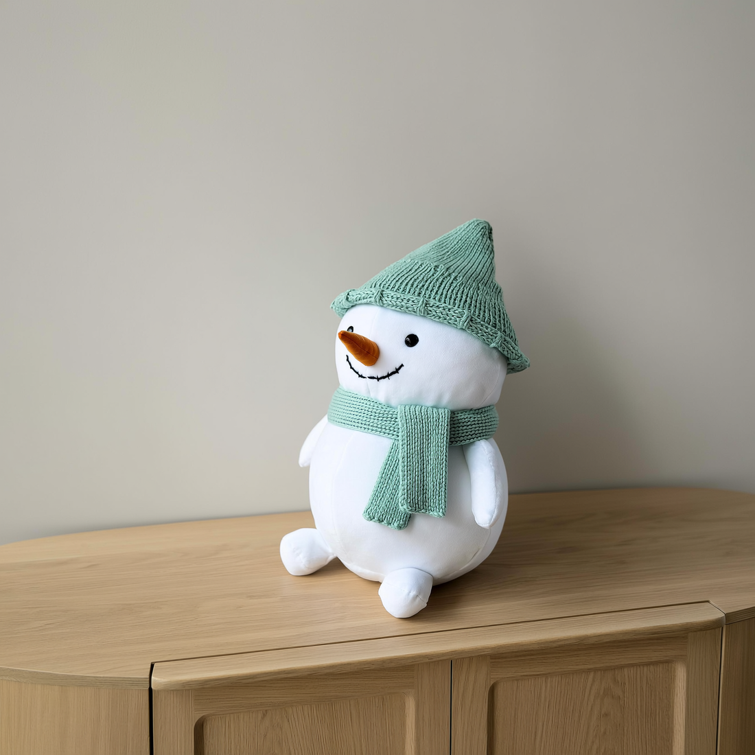Boneco de neve de pelúcia com touca e cachecol verdes sobre aparador de madeira — foto de ambiente 1